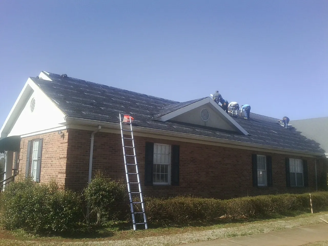 Crew tearing shingles off a brick ranch roof with a ladder set — Emergency Roof Repair work by our crew in Frederick