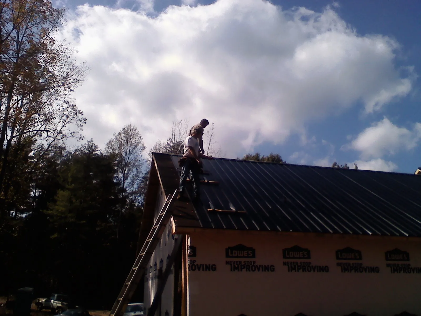 Roofer fastening dark metal panels high against a cloudy sky, from a Roof Inspection job in Frederick